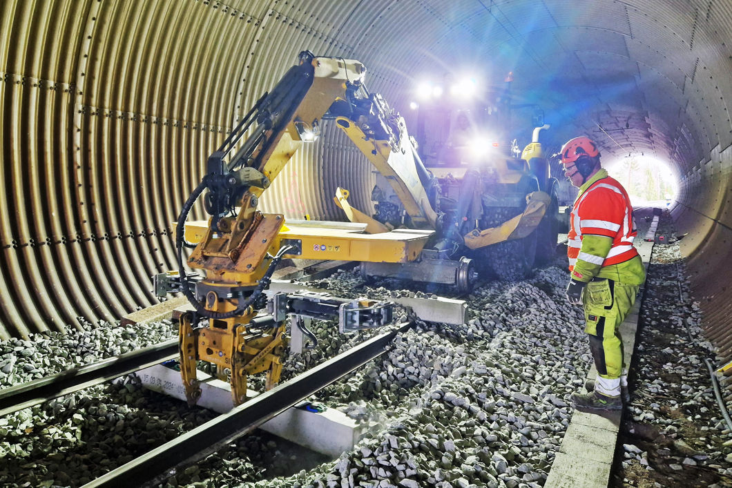 En arbeidsmaskin jobber i sporet inne i en tunnel. Mann i vernetøy sjekker at arbeidet går bra.