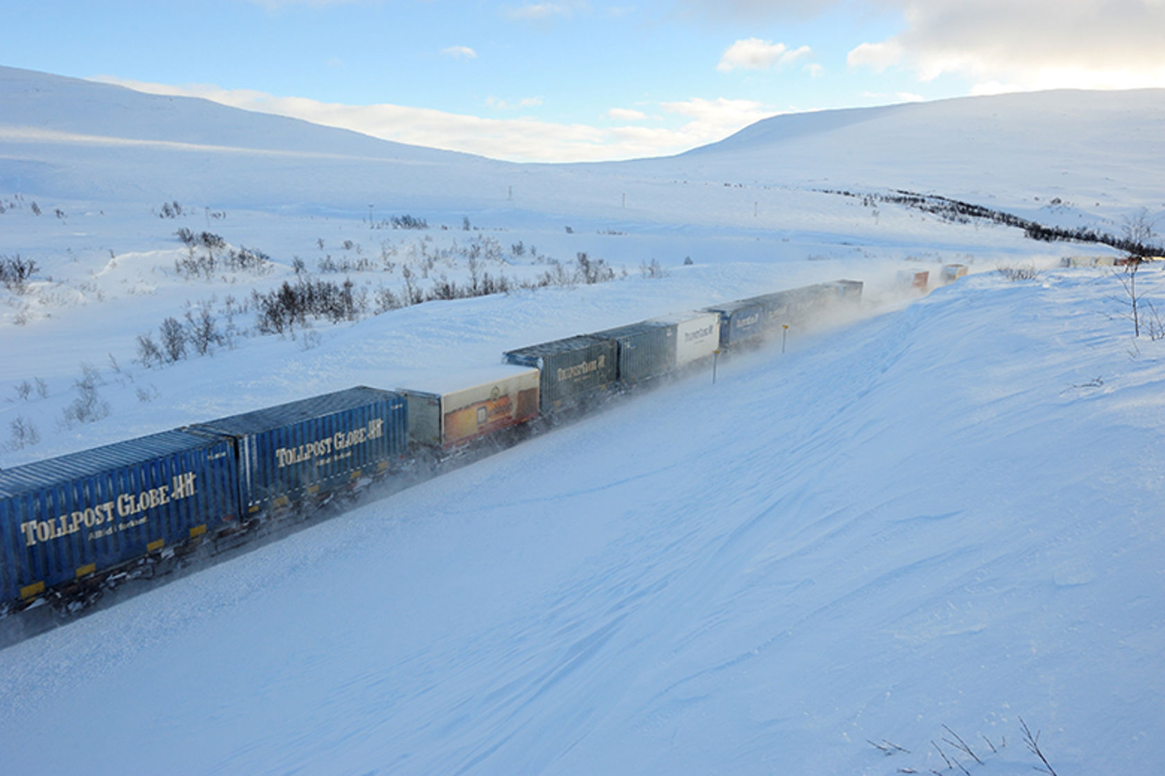 Godstog med mange godsvogner kjører over et snødekt fjell