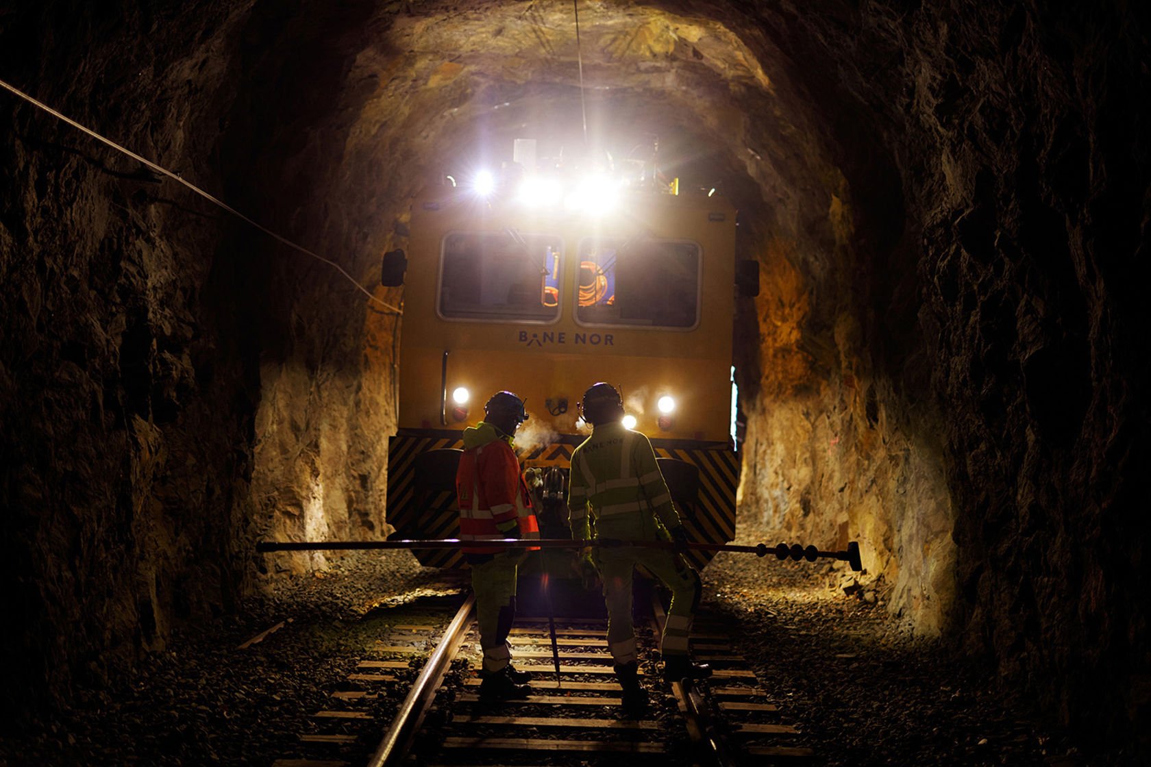 Skinnegående arbeidsmaskin i tunnel, to personer jobber i sporet.