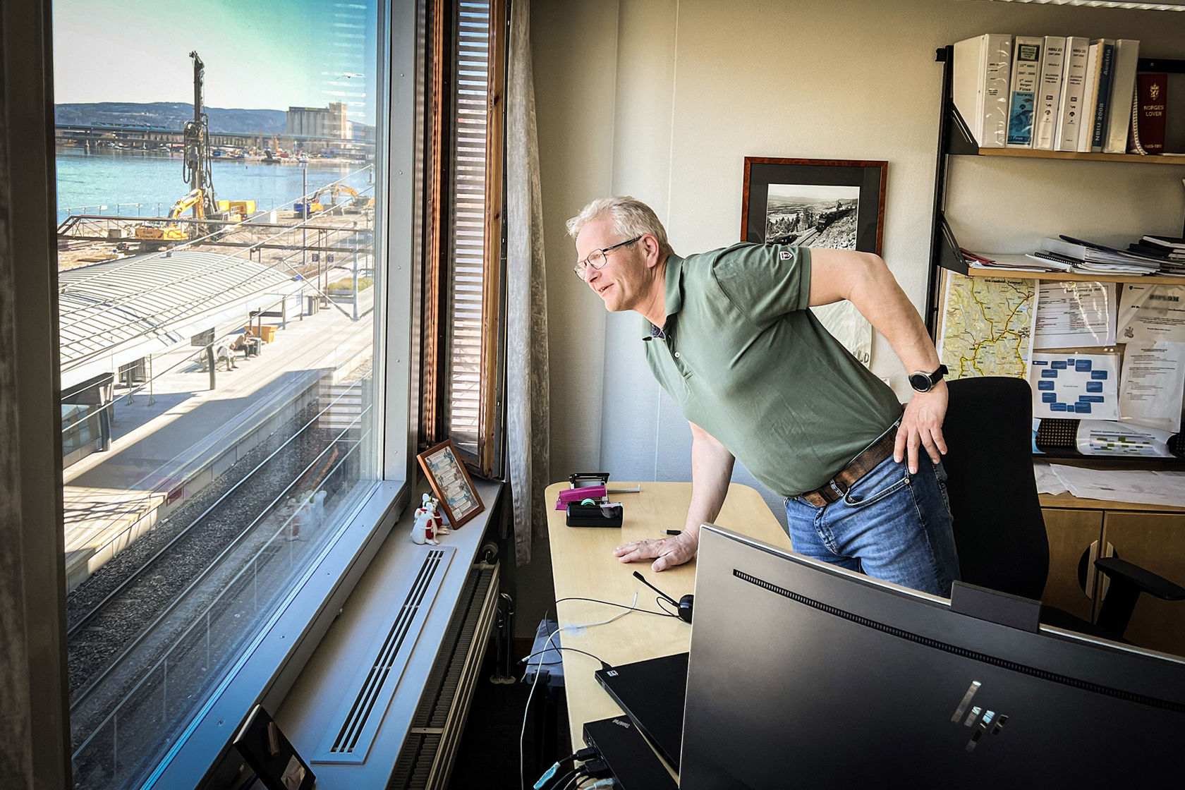 Mann lener seg over skrivebordet på sitt kontor og ser ut over stasjonsområdet utenfor vinudet.
