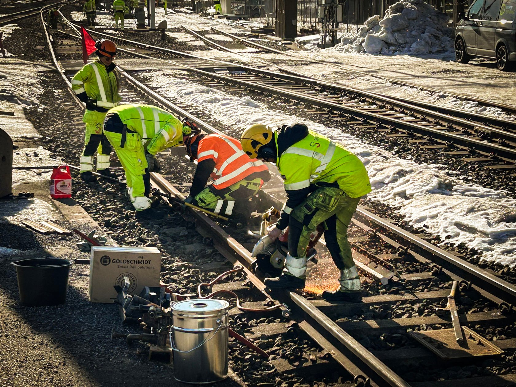 Fire arbeidere i vernetøy står i sporområdet. Den forreste av dem kapper skinner. Det er snø.