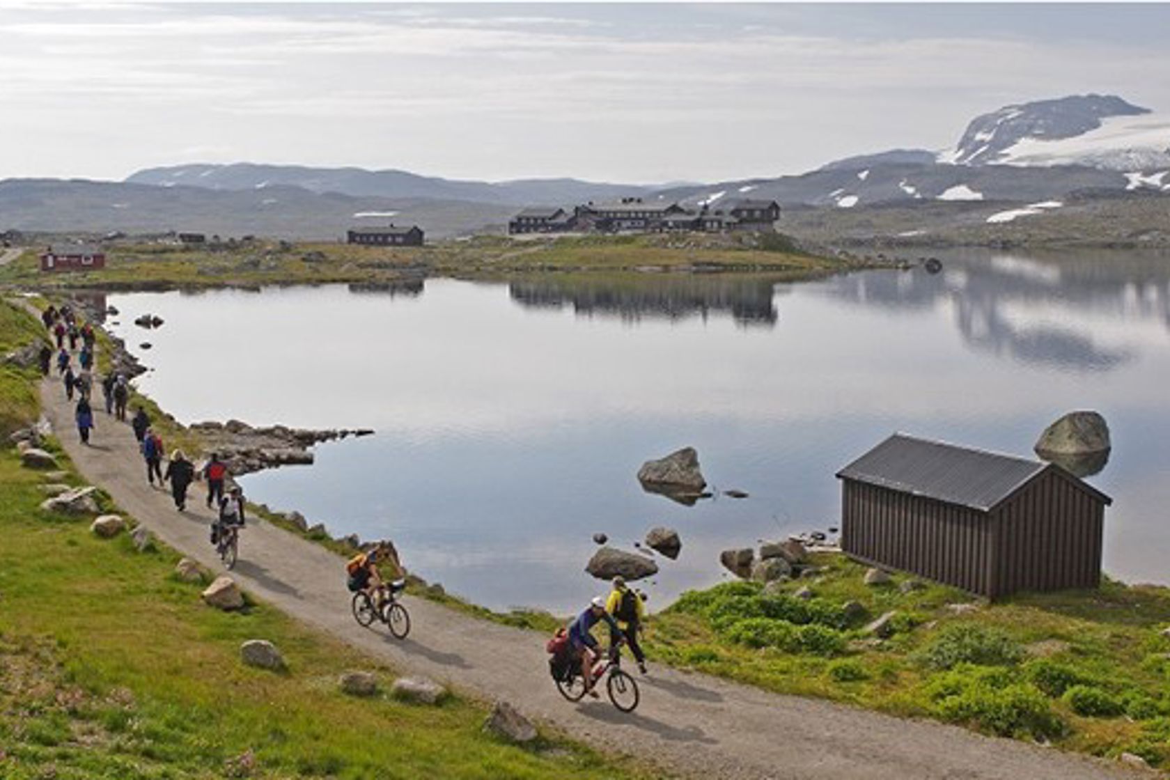 Utsynsbilete langs Rallarvegen med syklistar langs eit fiskevatn.