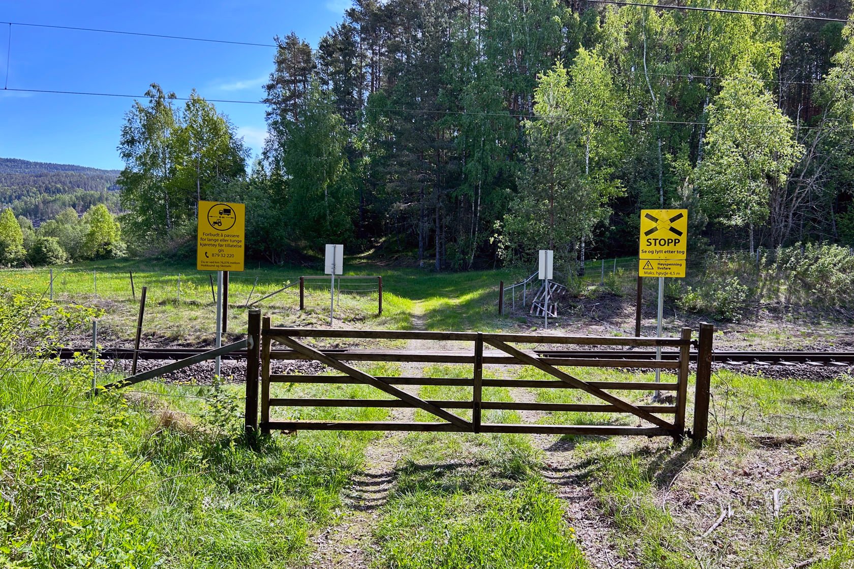 Bilde av en grind foran en enkel planovergang på jernbanen i landlige omgivelser.