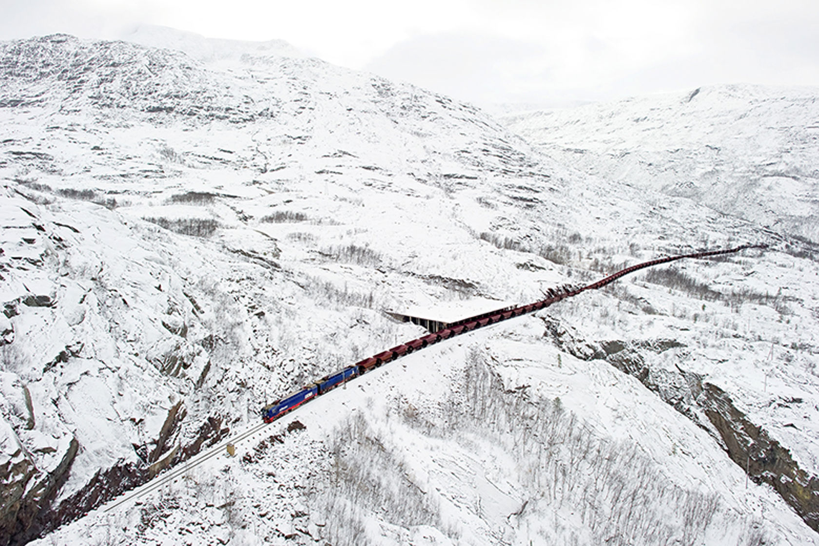 Et langs godstog passerer over jernbanen på en vidde om vinteren