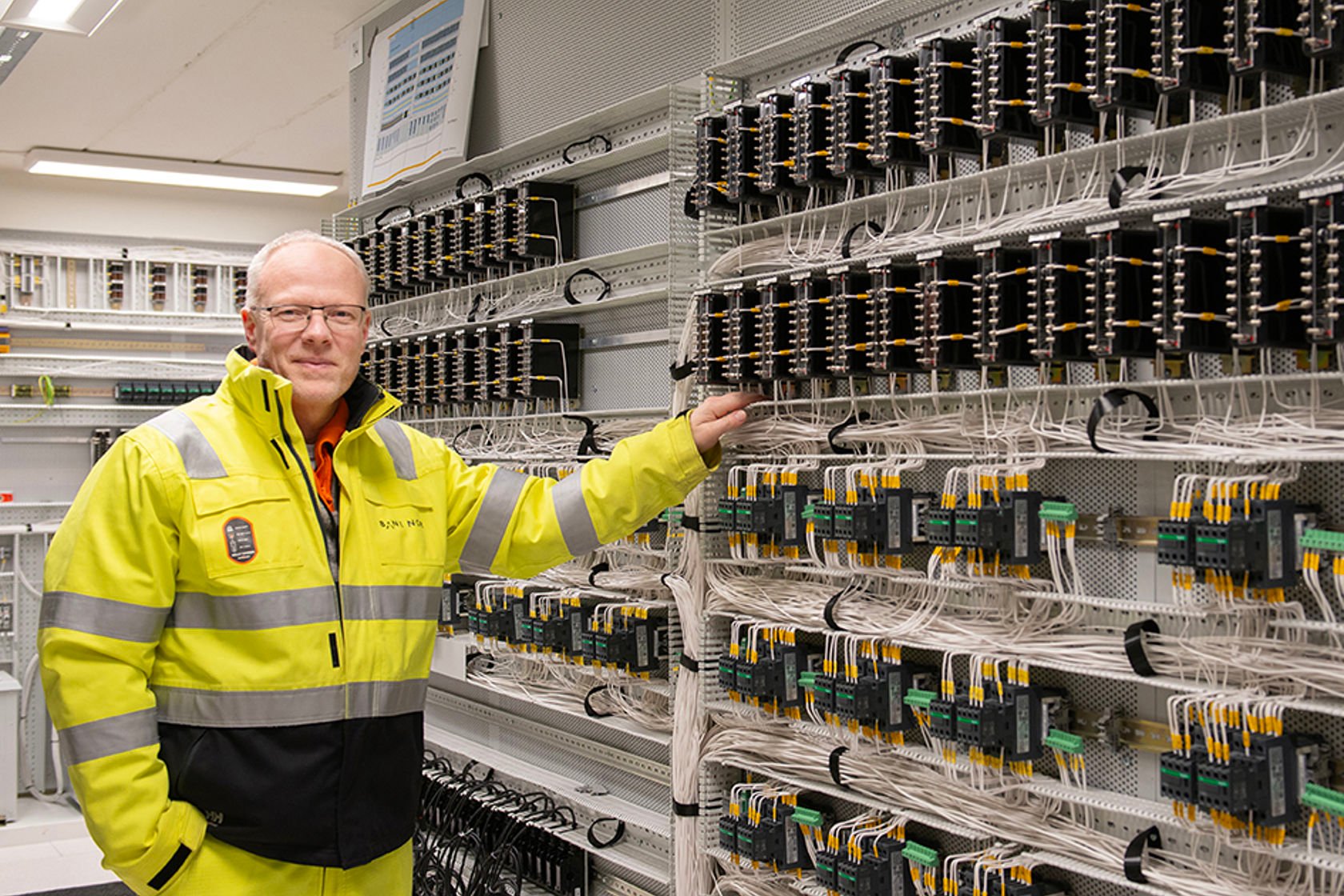 Bilde av mann i vernetøy i et rom med veldig mange ledninger.