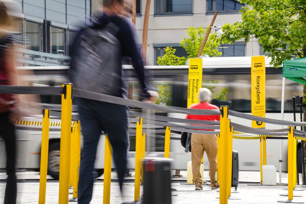 En mann går mellom noen gule sperrebånd som leder fram til en bussholdeplass.