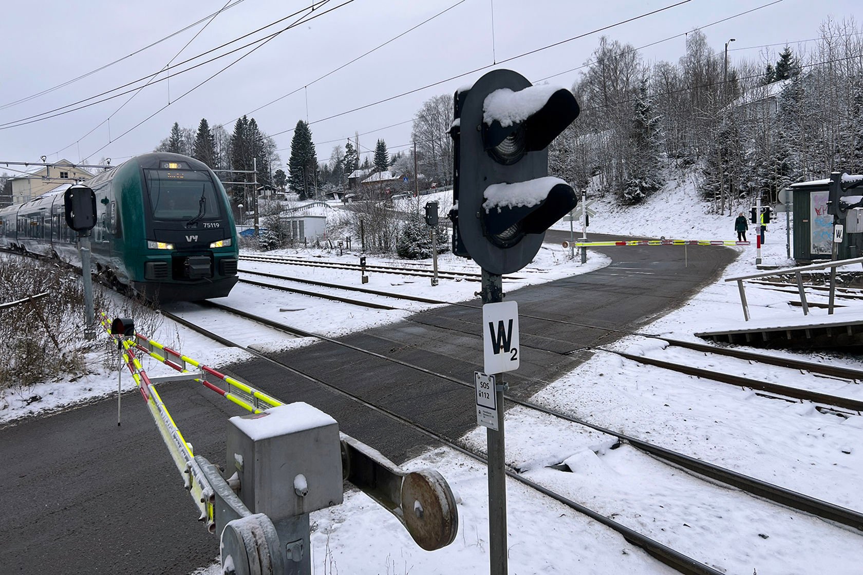 Bommene er nede og et tog er i ferd med å kjøre ut på planovergangen.