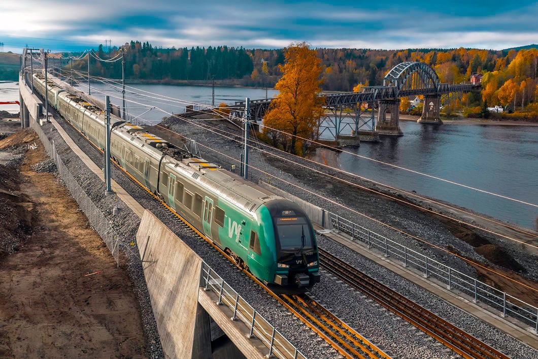 Et grønt tog i forgrunnen med Vorma, ny og gammel jernbanebru i bakgrunnen.