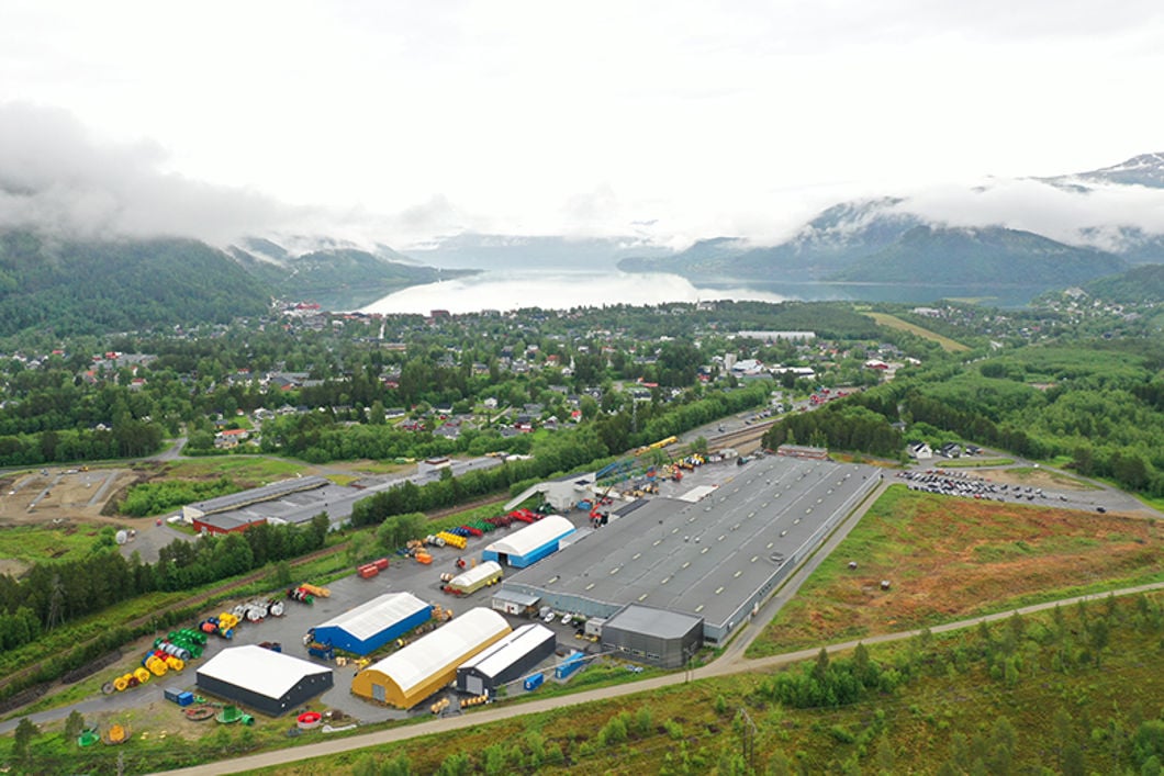 Bilde tatt ovenfra av stor bygning i et industriområde, med fjell og fjord i bakgrunn.