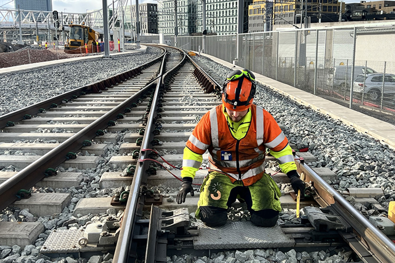 Mann i gult og oransje arbeidstøy jobber i jernbanespor.